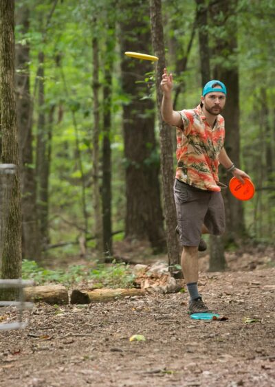 man throwing frisbee towards camera in the forrest
