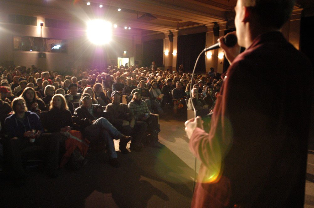 Speaker on Stage in front of a Crowd of Seated People