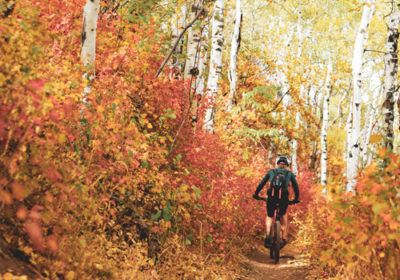 Mountain Biker Peddling Up-Hill on Trail Surrounded by Orange and Yellow Aspens in Fall