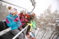 A Group of 4 Friends on a Chairlift with Snowy Trees in the Background