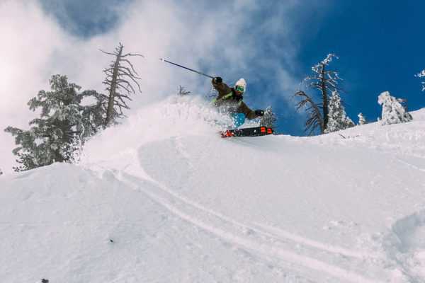 man skiing donwhill through fresh powder on a blue bird day